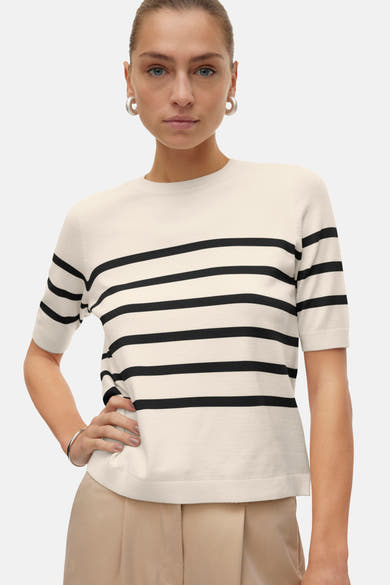 Pull écru à rayures noires de VERO MODA®, porté avec un pantalon beige et des boucles d'oreilles argentées.