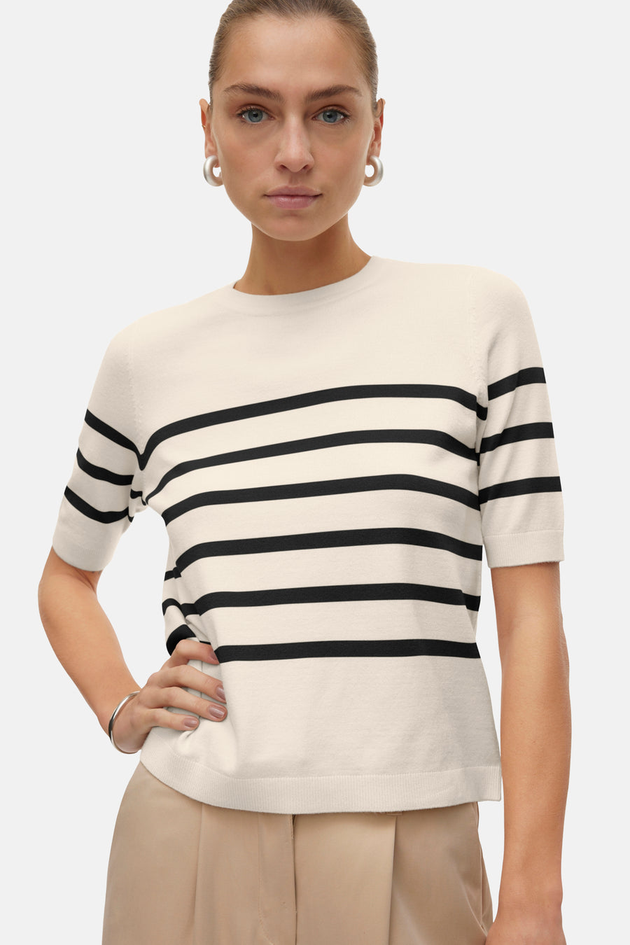Pull écru à rayures noires de VERO MODA®, porté avec un pantalon beige et des boucles d'oreilles argentées.