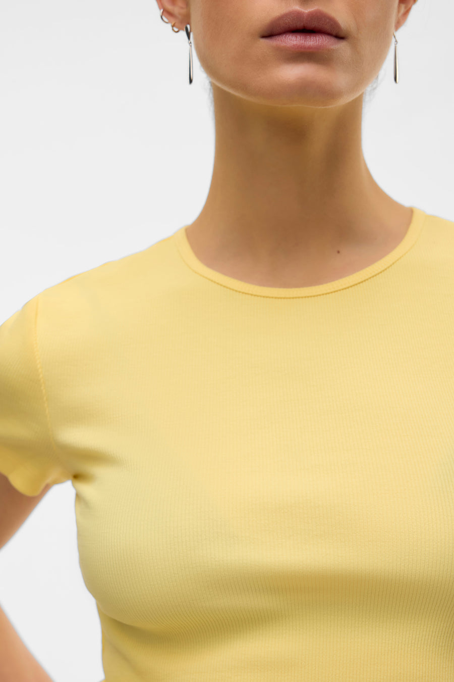 T-shirt jaune à manches courtes de Vero Moda, en maille côtelée, porté avec des boucles d'oreilles argentées.
