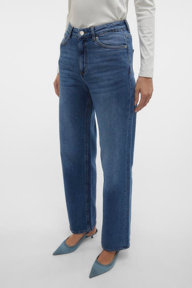 Jeans larges bleu moyen de Vero Moda, portés avec un haut blanc à manches longues et des escarpins bleus pointus.