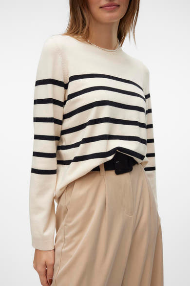 Pull écru à col rond de Vero Moda avec rayures horizontales noires, porté avec un pantalon beige taille haute et une ceinture noire.