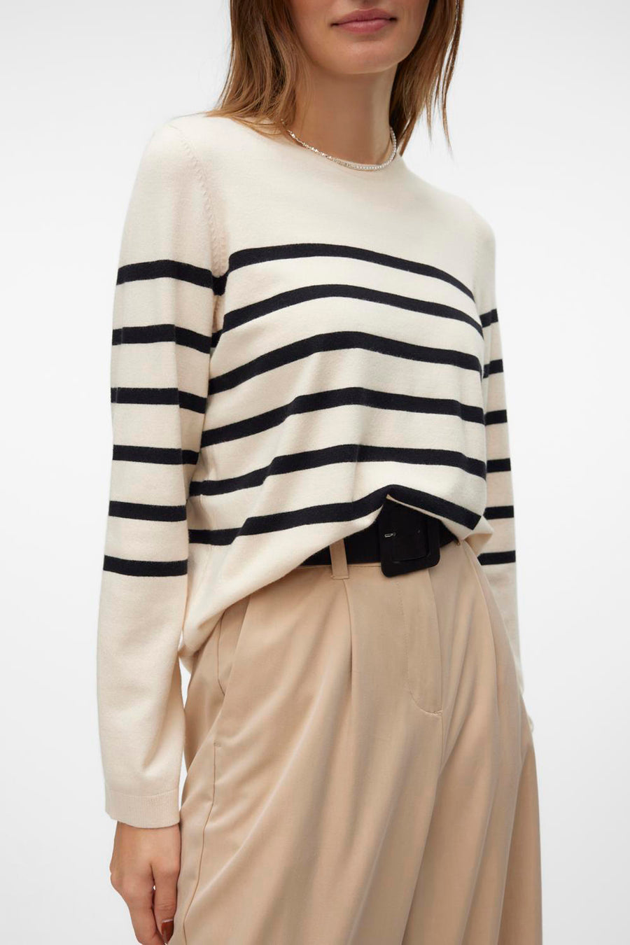 Pull écru à col rond de Vero Moda avec rayures horizontales noires, porté avec un pantalon beige taille haute et une ceinture noire.