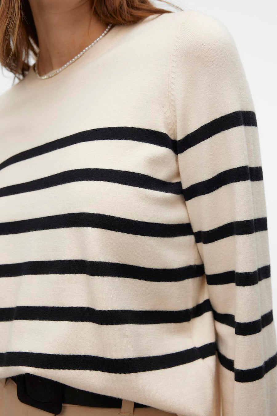 Pull à col rond écru de VERO MODA® avec rayures horizontales noires, porté avec un collier de perles.
