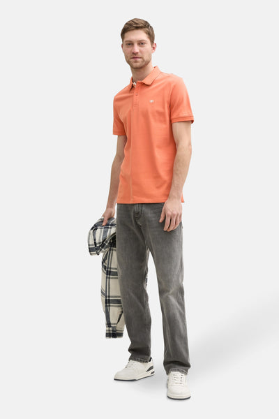 Oranje poloshirt met korte mouwen van Tom Tailor, gedragen met een grijze jeans en witte sneakers, geruit overhemd in de hand.