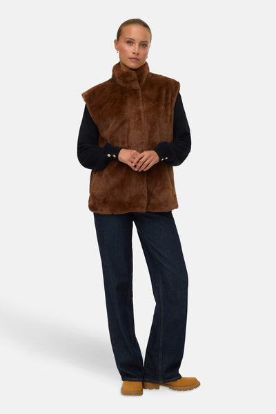 Veste sans manches marron en fausse fourrure de VERO MODA, portée sur un pull noir et un jean ample.