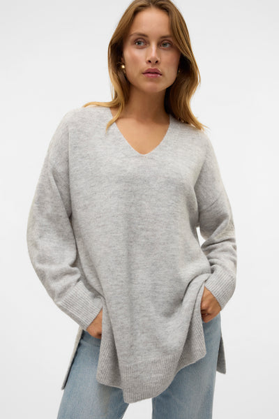 Pull à col en V gris de VERO MODA, porté avec un jean bleu clair, les mains dans les poches.