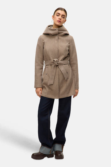 Lange beige jas van VERO MODA, met strikceintuur, capuchon en gedragen over een wijde marineblauwe jeans en bruine enkellaarsjes.