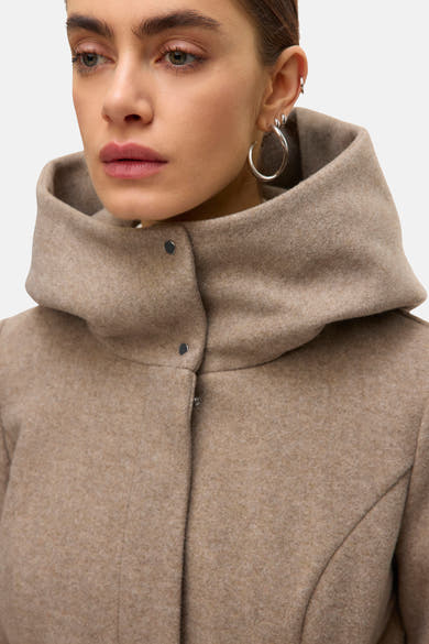 Lange beige jas van VERO MODA, met een opstaande kraag met knopen en zilveren oorbellen gedragen door het model.
