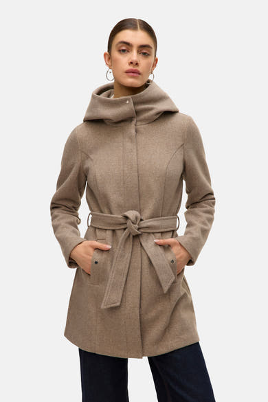 Lange beige jas van VERO MODA® met capuchon en strikceintuur, handen in de zakken, gedragen over een donkerblauwe jeans.