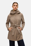 Lange beige jas van VERO MODA® met capuchon en strikceintuur, handen in de zakken, gedragen over een donkerblauwe jeans.