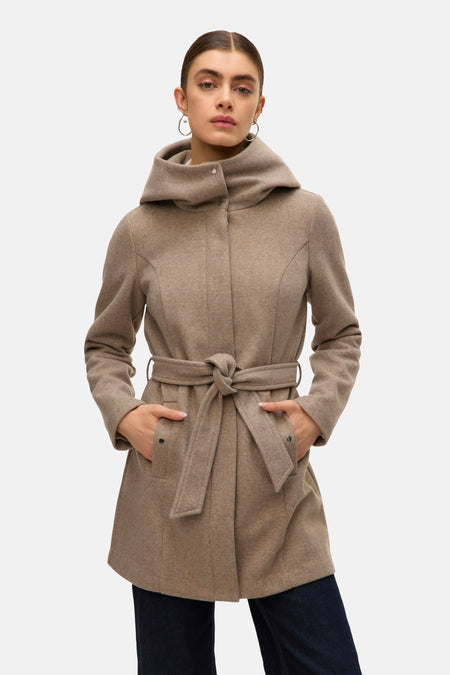 Lange beige jas van VERO MODA® met capuchon en strikceintuur, handen in de zakken, gedragen over een donkerblauwe jeans.