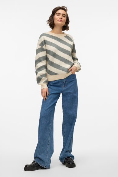 Pull à col rond beige de Vero Moda avec motif rayé et porté avec un jean bleu ample.
