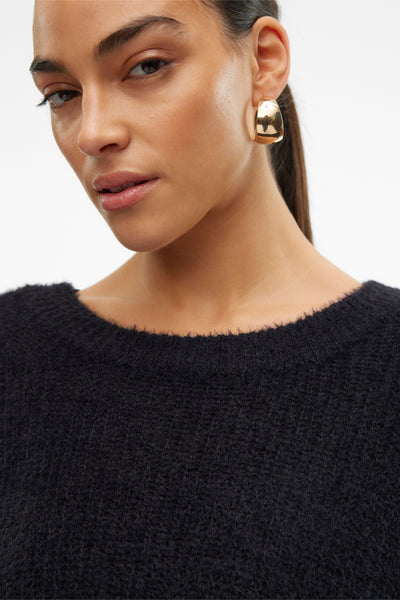 Zwarte trui met ronde hals van Vero Moda, in pluizige breinaald, gedragen met gouden oorbellen.