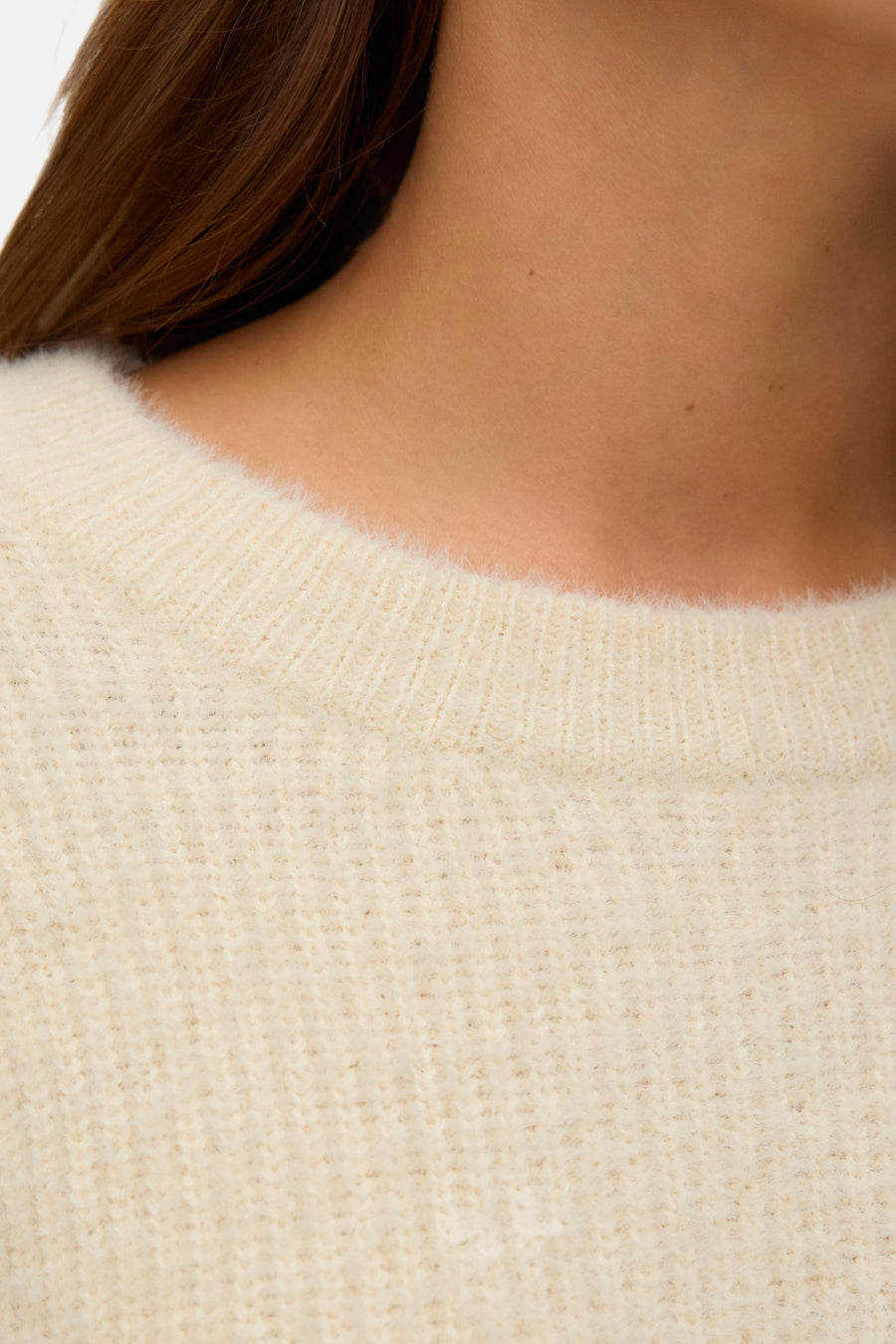 Crèmekleurige trui met ronde hals van VERO MODA, met gebreide textuurdetails, met gedeeltelijk zichtbare bruine nek en haar.