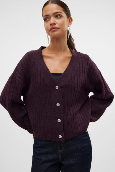Cardigan bordeaux en maille côtelée de Vero Moda, avec boutons décoratifs et porté sur un haut noir et un jean.
