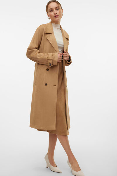 Veste longue marron de VERO MODA avec double boutonnage, portée avec une jupe et des escarpins clairs.