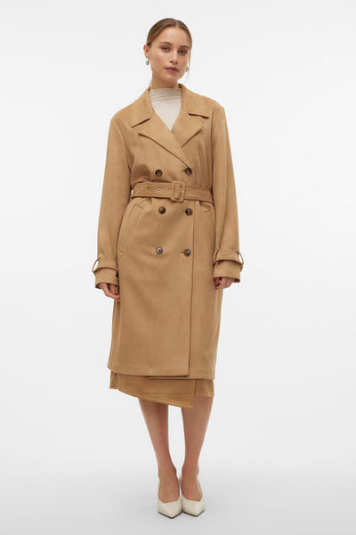 Lange bruine jas van VERO MODA, met een riem en knopen, gedragen over een beige rok en witte pumps.