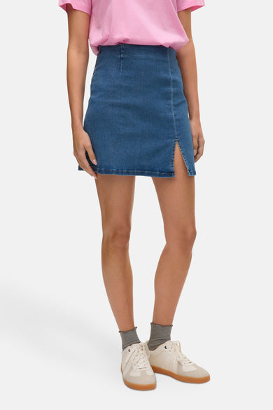 Jupe courte en denim bleu moyen de VERO MODA, avec fente et ourlet droit, portée avec des chaussettes grises et des baskets crème.