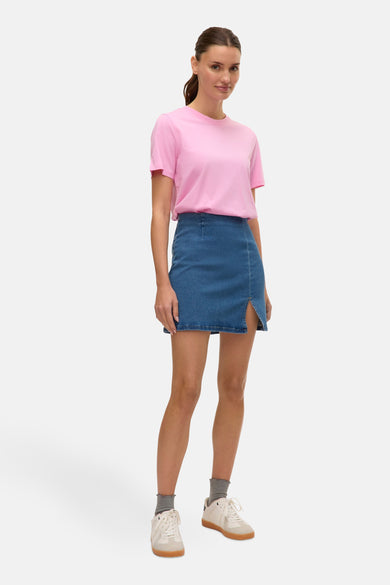 Jupe courte en denim bleu, de VERO MODA, avec une fente et portée avec un t-shirt rose.