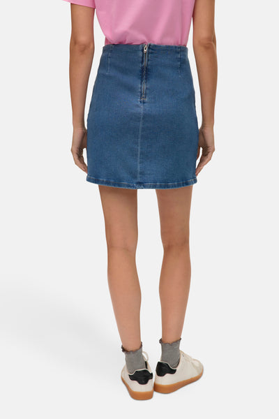 Jupe courte en denim bleu moyen de VERO MODA, avec fermeture éclair à l'arrière, portée avec des baskets blanches et des chaussettes grises.