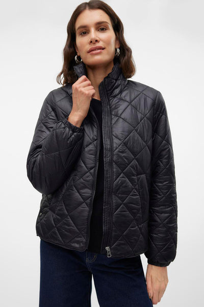 Veste courte noire de VERO MODA, matelassée en losanges, portée avec un pull noir et un jean.
