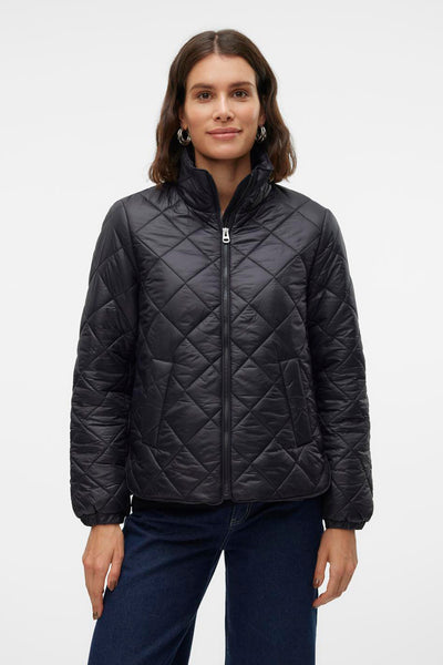 Veste courte noire par VERO MODA, matelassée avec fermeture éclair, portée avec un jean bleu foncé.

