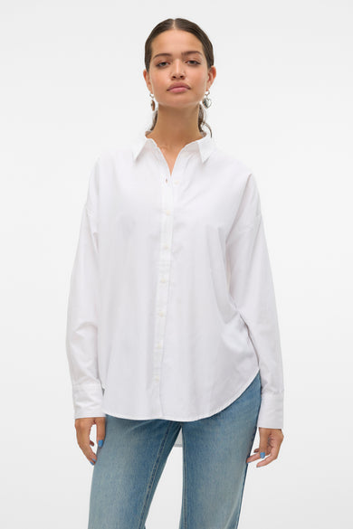Chemise blanche à manches longues de VERO MODA, portée avec un jean bleu clair et des boucles d'oreilles pendantes.
