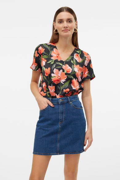 T-shirt à manches courtes multicolore de Vero Moda, à motif floral sur fond noir, porté avec une jupe en jean.
