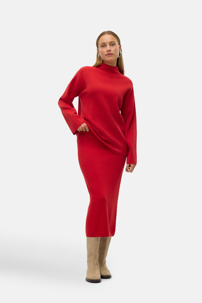 Jupe rouge mi-longue par VERO MODA® portée avec un pull rouge assorti et des bottes en daim.