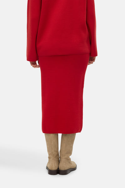 Jupe midi rouge de VERO MODA, portée avec un pull rouge assorti et des bottes en daim marron.