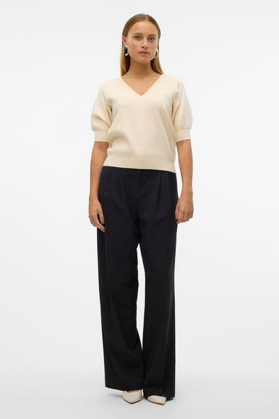 Ecru V-hals trui van VERO MODA, korte pofmouwen, gedragen met een wijde zwarte broek en beige schoenen.