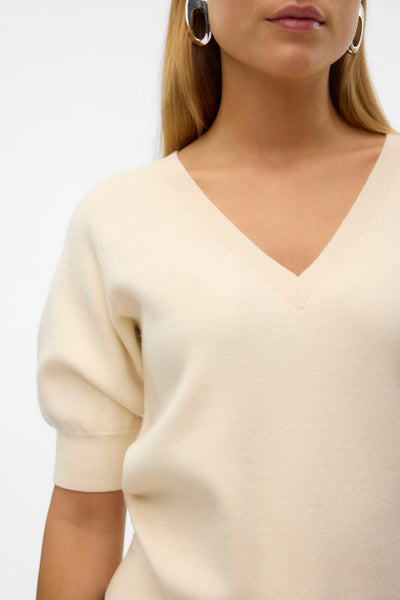 Pull à col en V écru de Vero Moda, porté avec des boucles d'oreilles argentées.