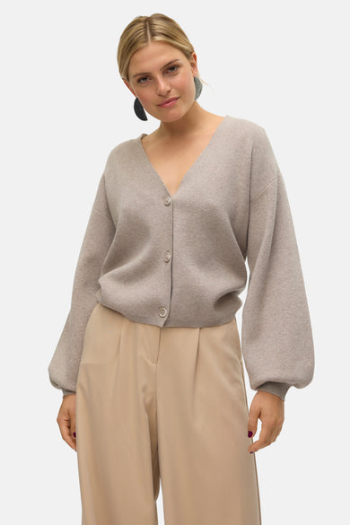 Cardigan beige de VERO MODA, avec des boutons, porté avec un pantalon beige et des boucles d'oreilles bleues.
