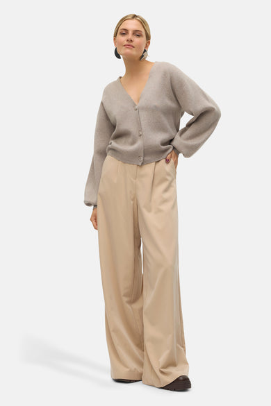 Cardigan beige de VERO MODA, porté avec un pantalon taille haute et des boucles d'oreilles rondes.