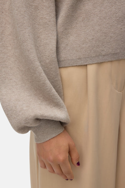 Cardigan beige de VERO MODA, manches longues bouffantes et coupe courte, porté avec un pantalon beige.
