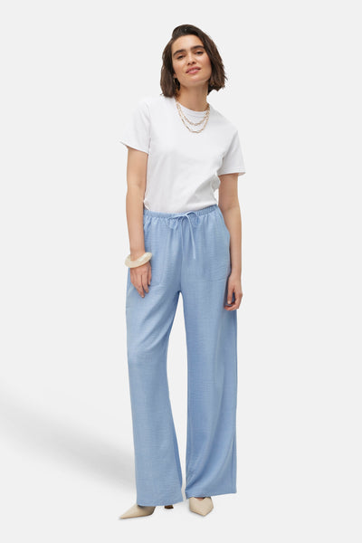 Pantalon coloré bleu de VERO MODA®, coupe ample avec cordon de serrage à la taille, porté avec un t-shirt blanc et des chaussures pointues.