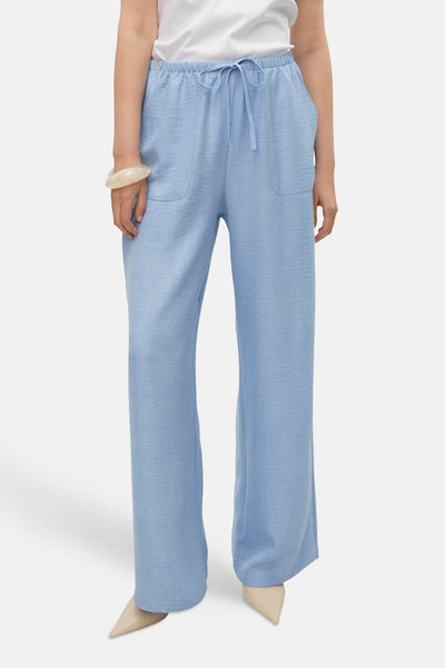 Pantalon coloré bleu par VERO MODA®, coupe ample, avec poches et cordon de serrage, porté avec un bracelet ivoire.