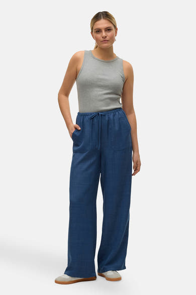 Pantalon coloré bleu de VERO MODA, avec cordon de serrage, porté avec un débardeur gris uni et des baskets.
