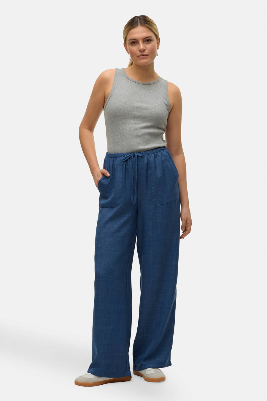Pantalon coloré bleu de VERO MODA, avec cordon de serrage, porté avec un débardeur gris uni et des baskets.

