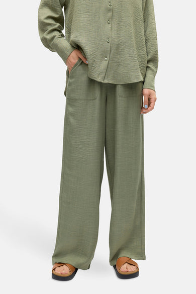 Pantalon vert ample de VERO MODA, avec poches et texture plissée, porté avec des sandales marron.

