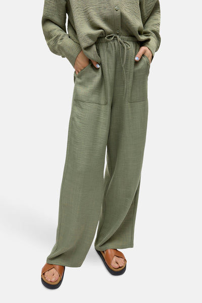 Pantalon coloré vert de VERO MODA, ample avec poches et cordon de serrage, porté avec des sandales marron.
