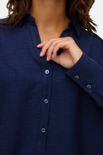 Pantalon coloré bleu de Vero Moda, porté avec une chemise bleu marine et des boutons assortis.