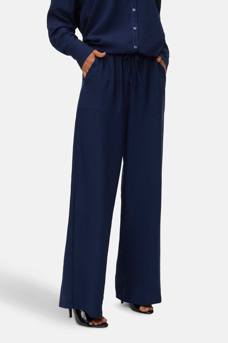 Pantalon coloré bleu de VERO MODA, avec poches et cordon de serrage, porté avec des talons hauts.