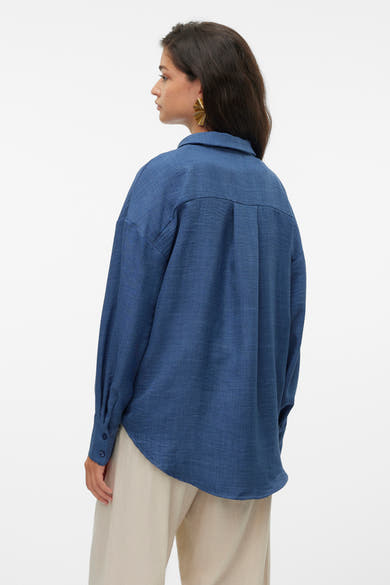 Chemise bleu à manches longues de VERO MODA, avec détails plissés au dos et porté avec un pantalon beige.