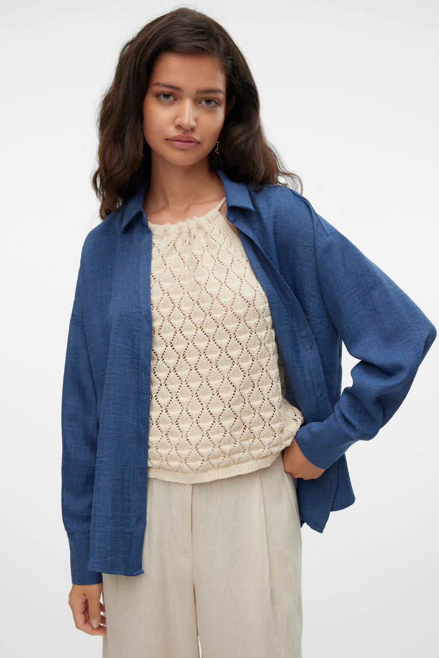 Chemise bleue à manches longues de VERO MODA®, portée ouverte sur un haut texturé et un pantalon beige.
