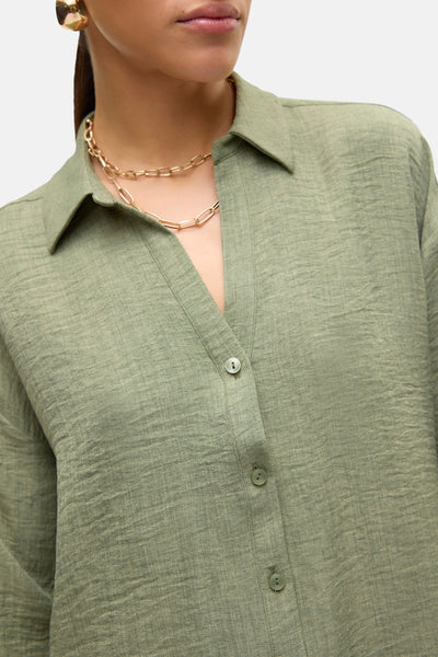 Chemise à manches longues verte de Vero Moda, avec une chaîne dorée au niveau du cou.