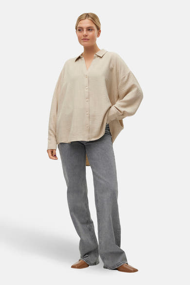 Chemisier beige à manches longues de VERO MODA, porté avec un jean gris et des chaussures marron.
