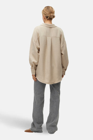Chemise beige à manches longues de VERO MODA, texturée, portée avec un jean gris et des chaussures marron, vue de dos.