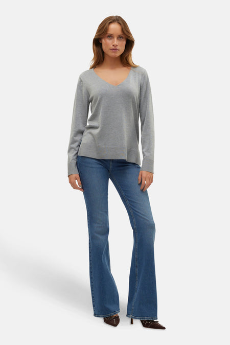 Grijze V-hals trui van VERO MODA, gedragen met een wijde jeans en bruine schoenen.