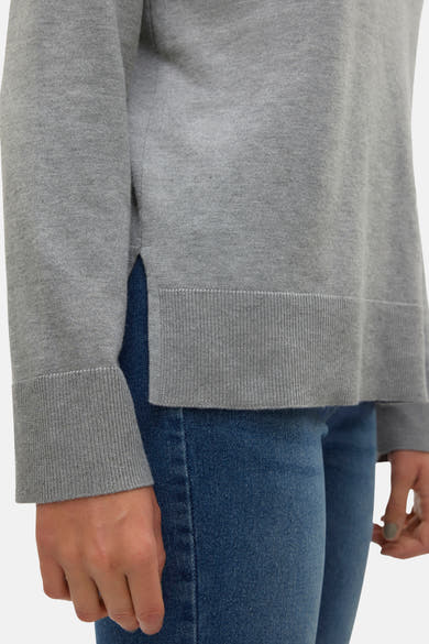 Pull col V gris de VERO MODA, avec ourlet côtelé et manches longues, porté avec un jean bleu classique.